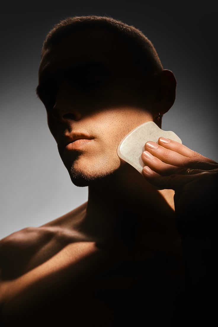 Close-up of a person using a gua sha tool on their jawline, illustrating inclusive and genderless skincare practices by IMEAN.