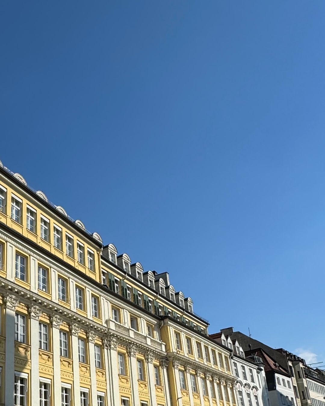 Historic yellow building with ornate white columns and classic European windows, bathed in golden sunlight under a clear blue sky – a visual from Sarah’s Edit to Munich, Germany – travel inspiration from IMEAN Beauty.