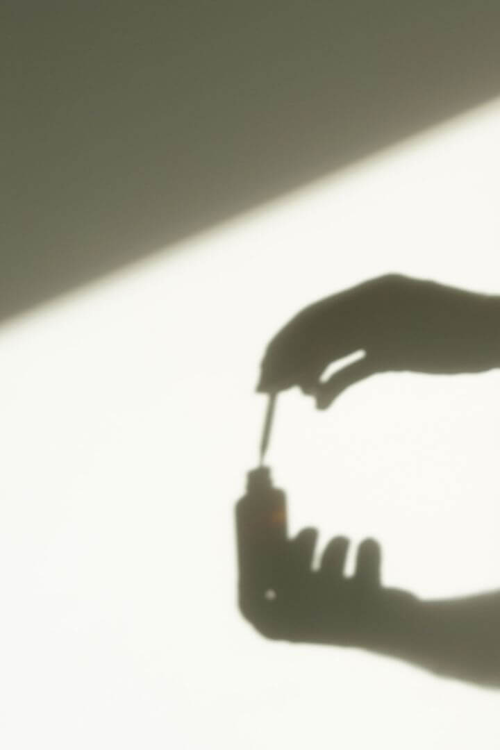 Silhouette of a hand holding a skincare dropper, symbolizing clean beauty and minimalist skincare routine